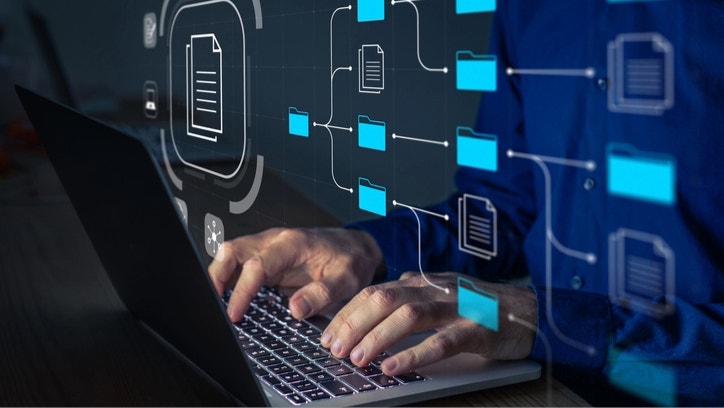 Document Management System (DMS) being setup by IT consultant working on laptop computer in office. Software for archiving, searching and managing corporate files and information. Business processes
